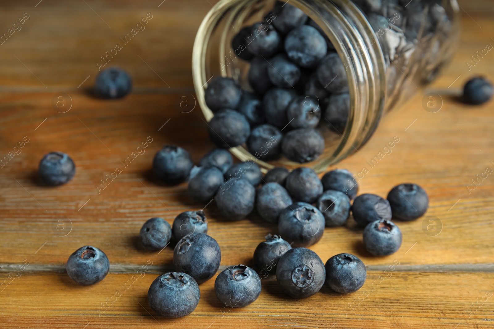 Photo of Overturned glass jar of ripe blueberries on wooden table, closeup