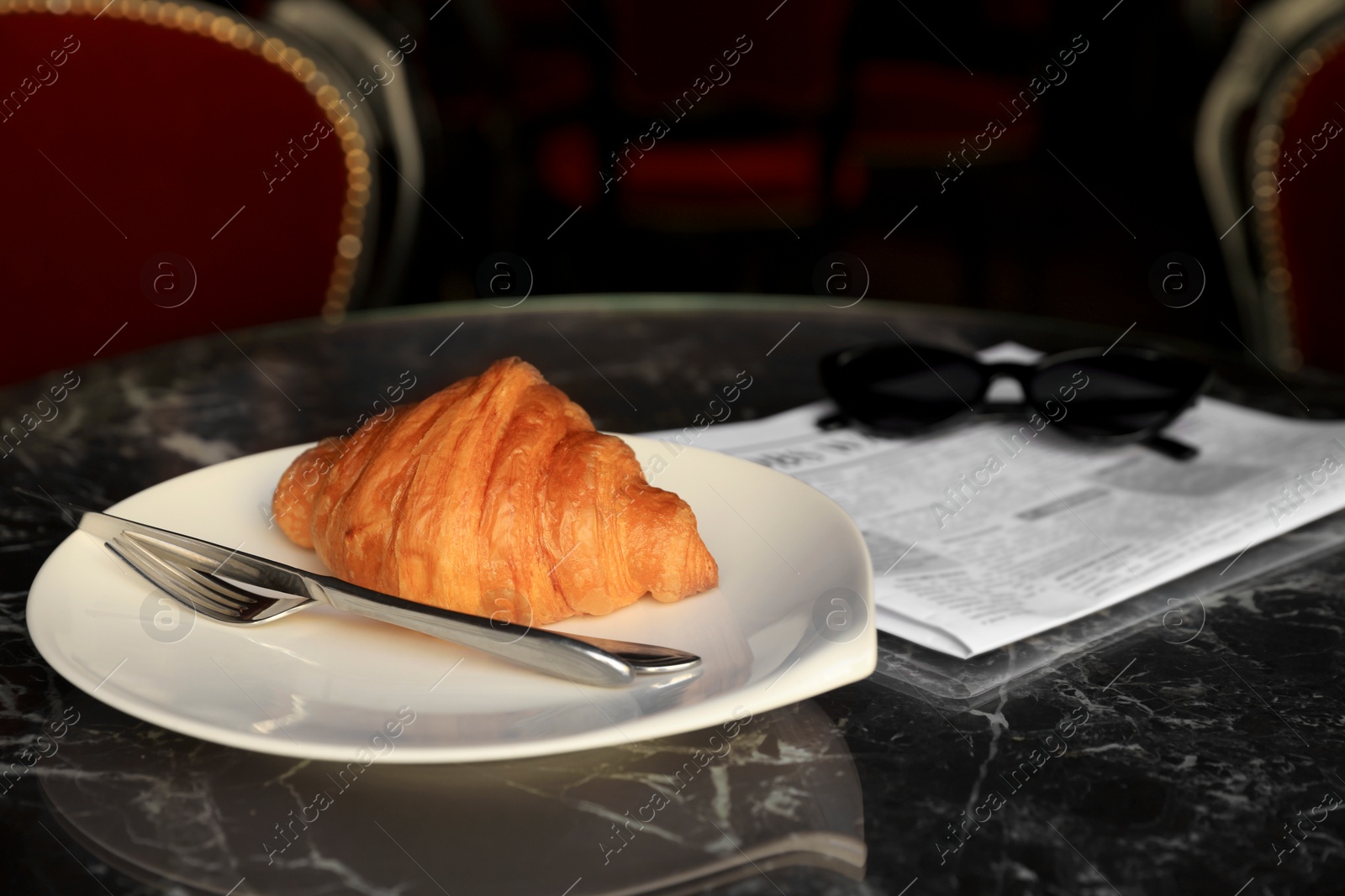 Photo of Tasty croissant, newspaper and sunglasses on black table