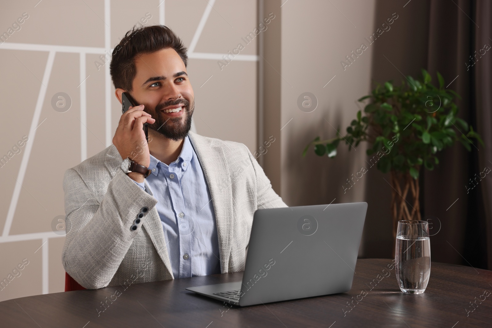 Photo of Happy man using modern laptop while talking on smartphone at table in office