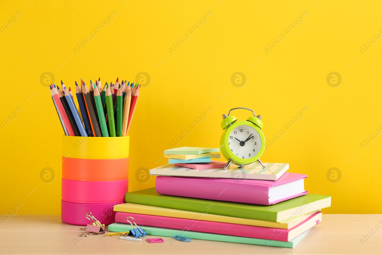 Photo of Different school stationery and alarm clock on table against yellow background. Back to school