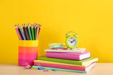 Photo of Different school stationery and alarm clock on table against yellow background. Back to school