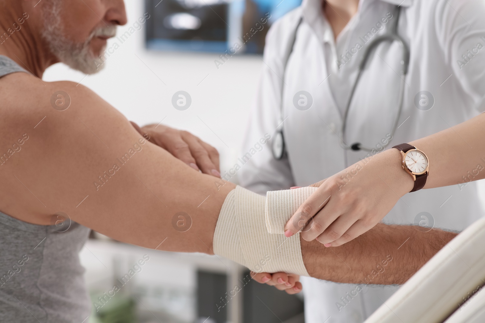 Photo of Orthopedist applying bandage onto patient's elbow in clinic, closeup