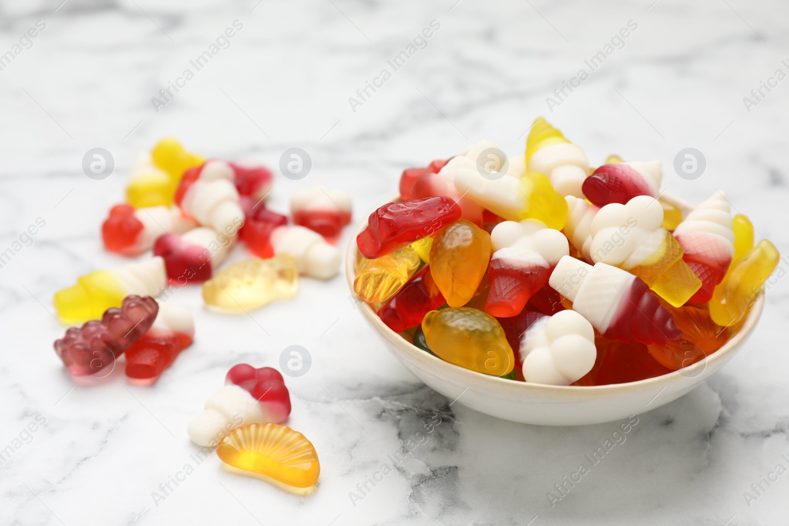 Photo of Many different delicious gummy candies on white marble table, closeup. Space for text