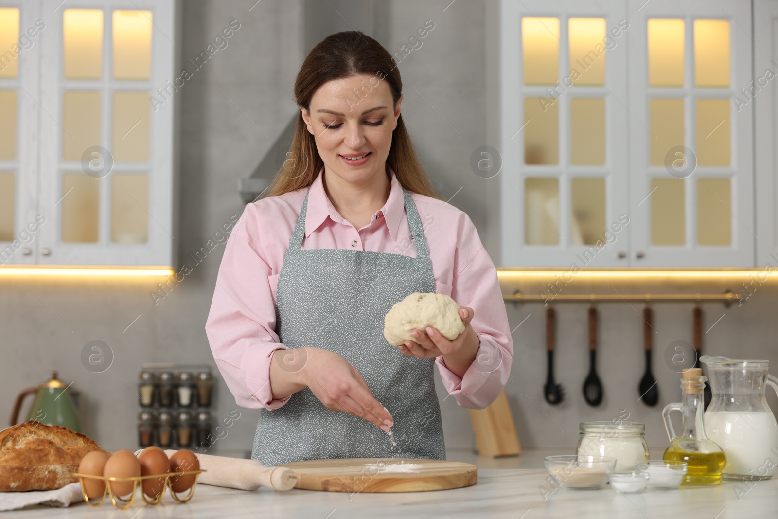 Photo of Making bread. Woman preparing raw dough at white table in kitchen