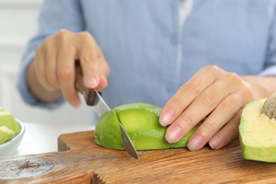 Photo of Woman cutting ripe avocado at table, closeup