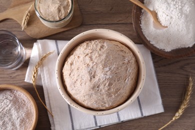 Photo of Fresh sourdough in proofing basket, flour and spikes on wooden table, flat lay