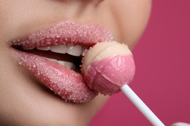 Young woman with beautiful lips covered in sugar eating lollipop on pink background, closeup