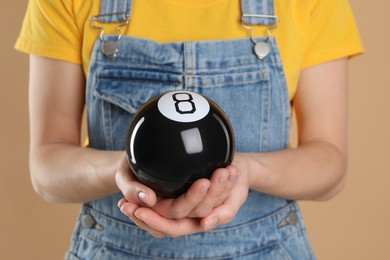 Photo of Woman holding magic eight ball on light brown background, closeup
