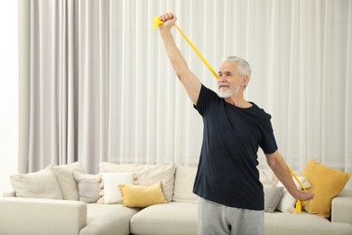 Photo of Senior man doing exercise with fitness elastic band at home. Space for text