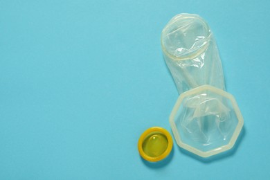 Photo of Unrolled female and male condoms on light blue background, flat lay with space for text. Safe sex