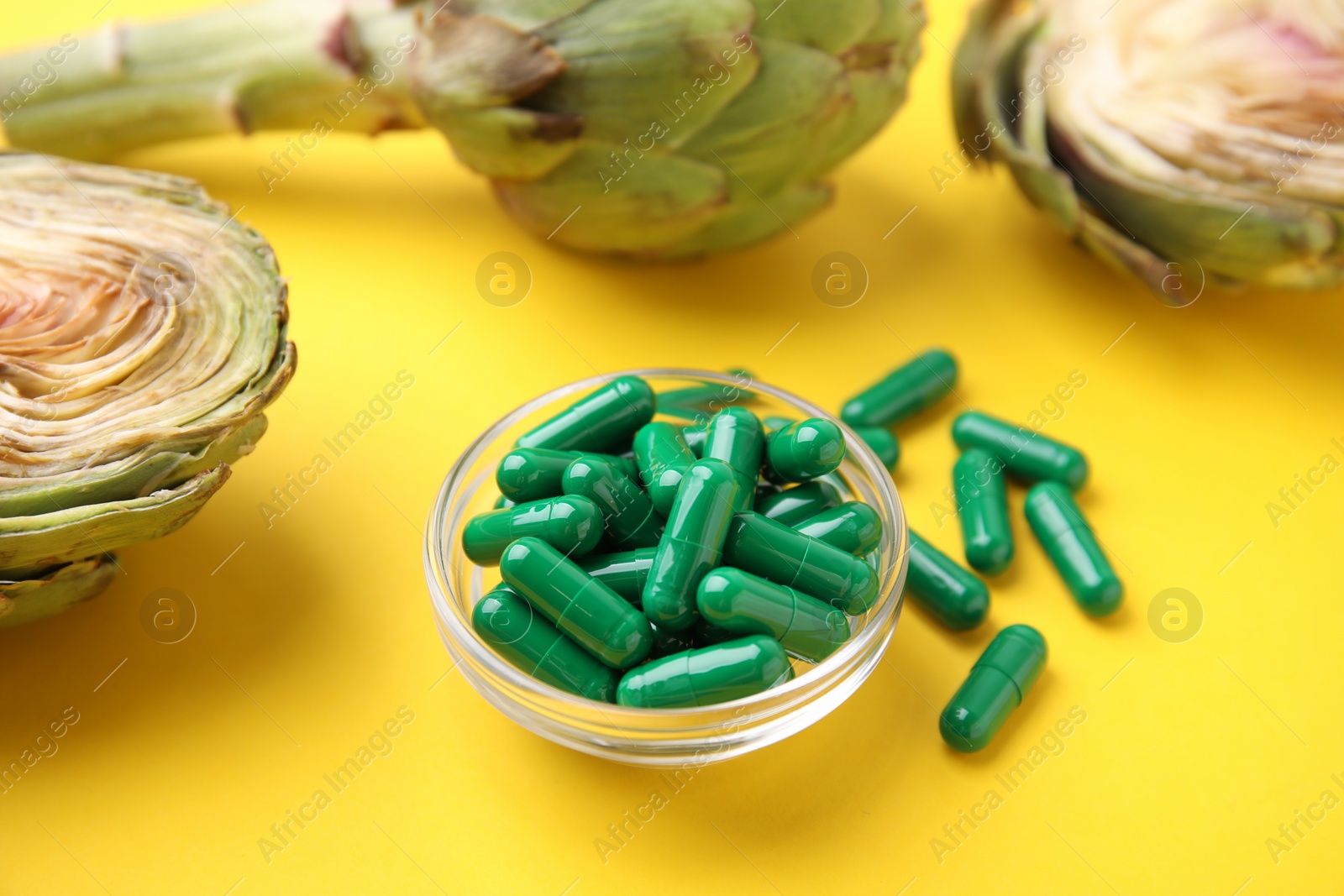 Photo of Bowl with pills and fresh artichokes on yellow background, closeup