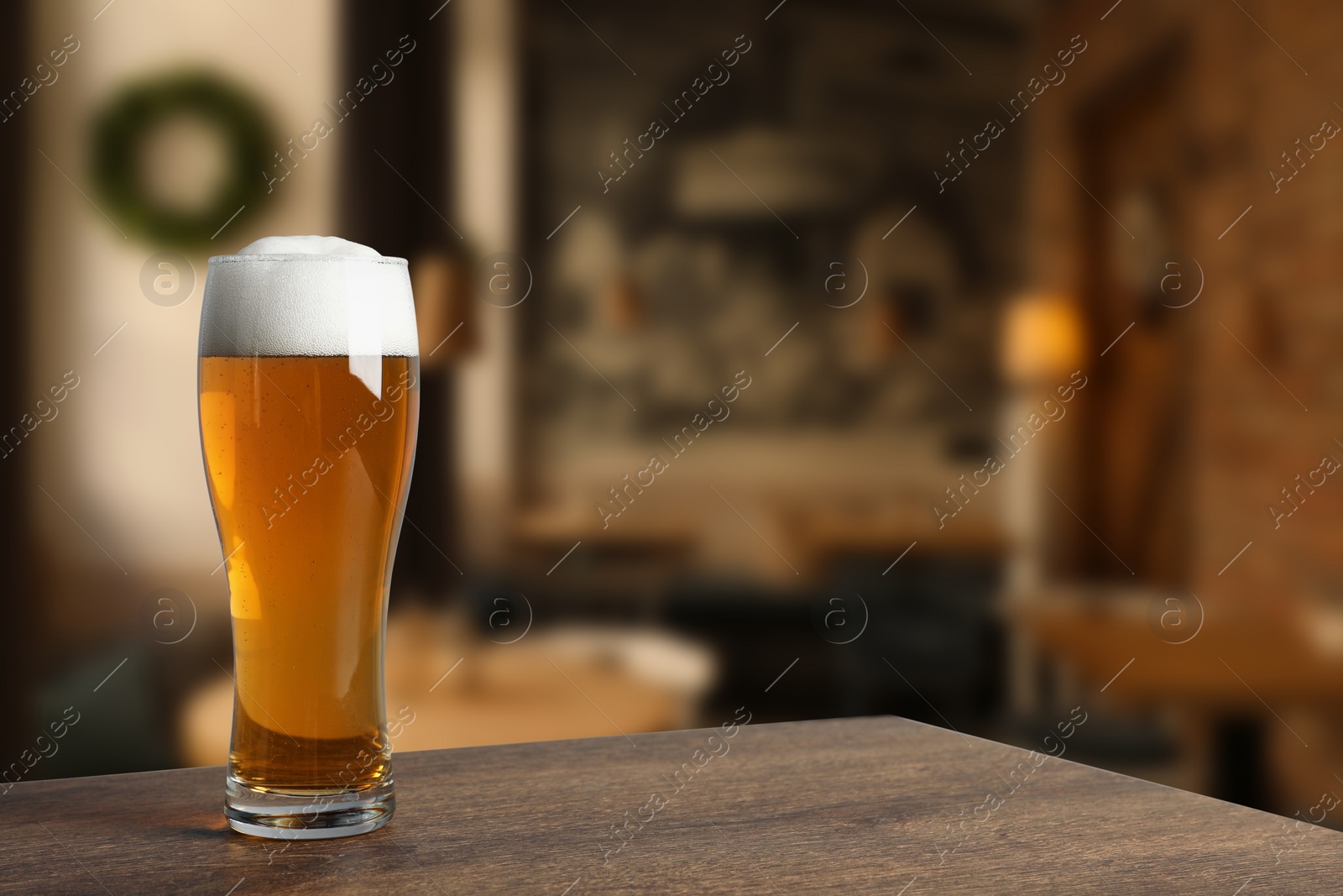 Image of Glass with fresh beer on wooden table in pub, space for text