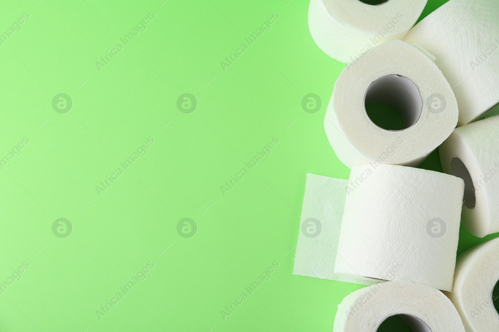 Photo of Soft toilet paper rolls on green background, flat lay. Space for text