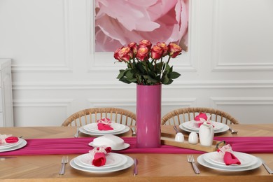 Color accent table setting. Plates, cutlery, pink napkins and vase with beautiful roses in dining room