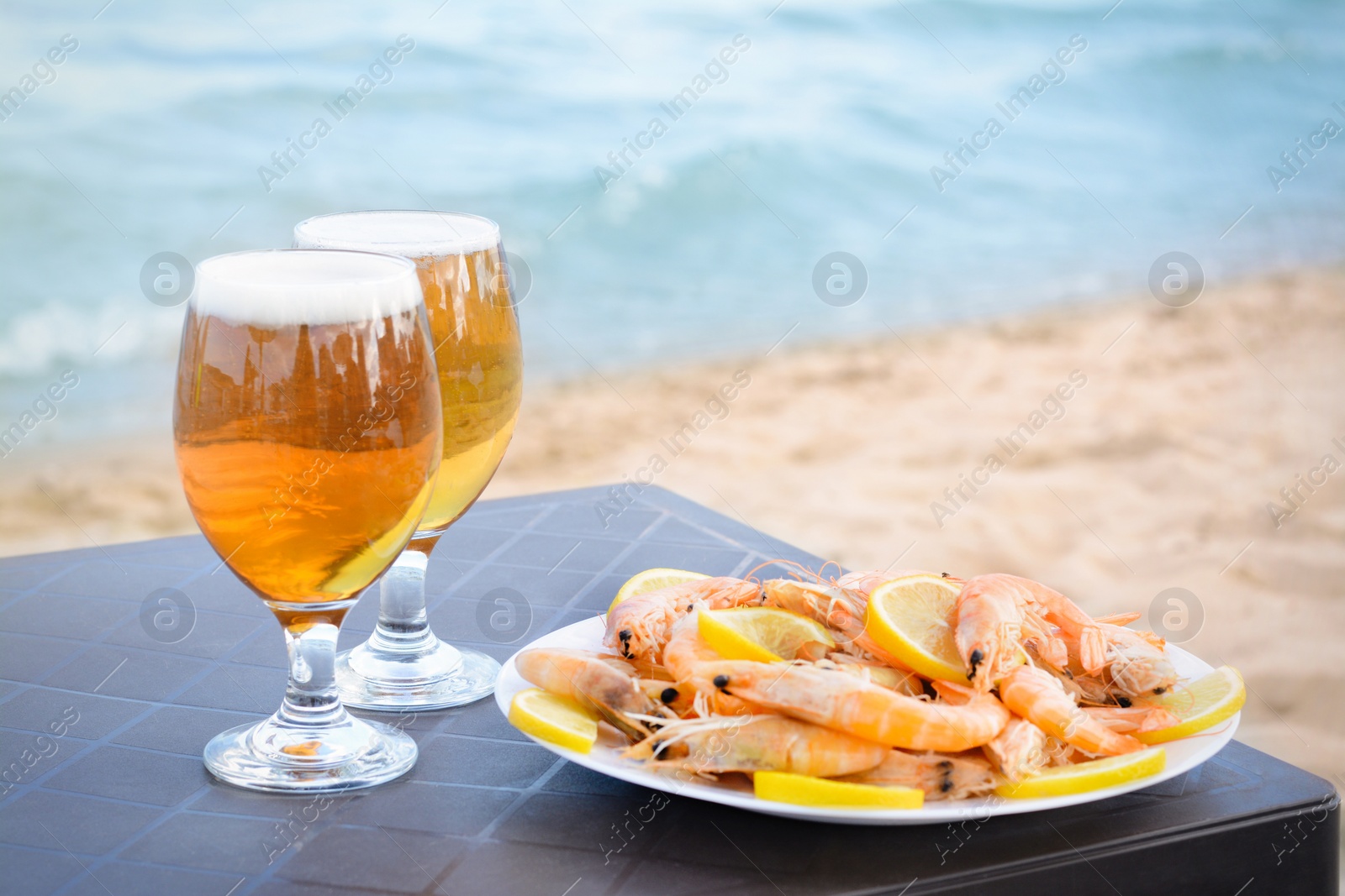 Photo of Cold beer in glasses and shrimps served with lemon on beach