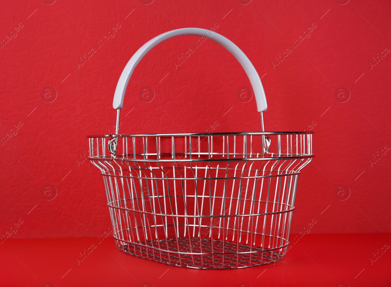 Photo of Empty metal shopping basket on red background