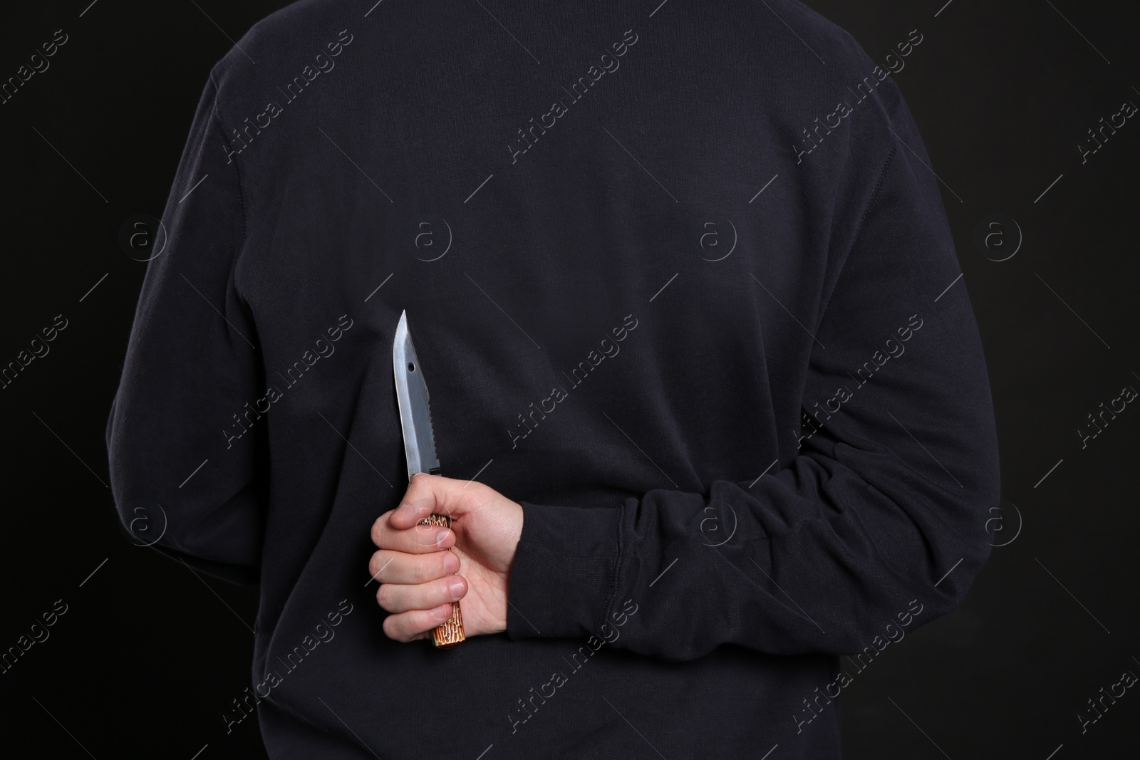 Photo of Man with knife behind his back on black background, closeup. Dangerous criminal