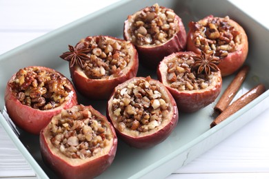 Tasty baked apples with nuts, honey and spices in dish on white table, closeup