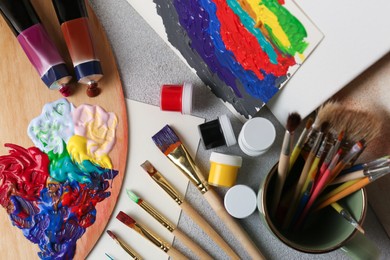 Artist's palette with mixed bright paints and brushes on textured table, flat lay