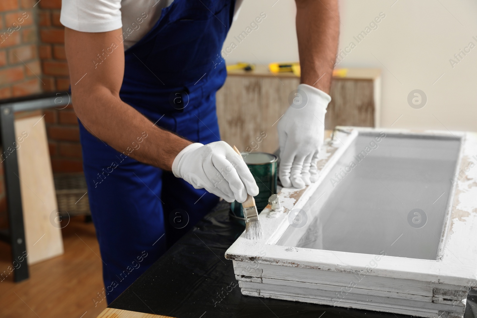 Photo of Repairman painting old window at table indoors, closeup