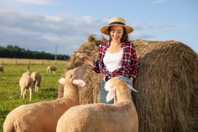 Photo of Smiling woman and sheep near hay bale on animal farm