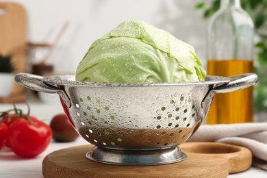 Photo of Wet cabbage in colander on white table, closeup