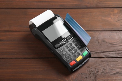 Photo of Modern payment terminal with credit card on wooden background