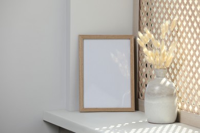 Photo of Blank photo frame and vase with dried plant on white window sill. Space for text