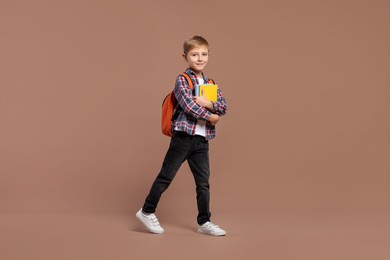 Photo of Happy schoolboy with backpack and books on brown background