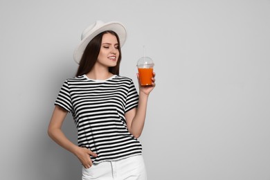 Photo of Beautiful young woman with plastic cup of juice on light grey background. Space for text