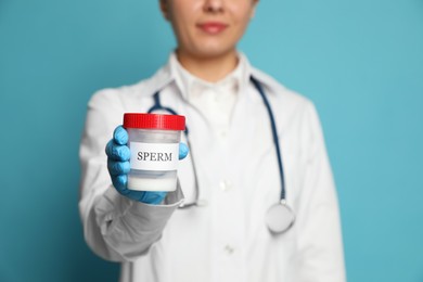 Doctor holding container with sperm on turquoise background, closeup. Space for text