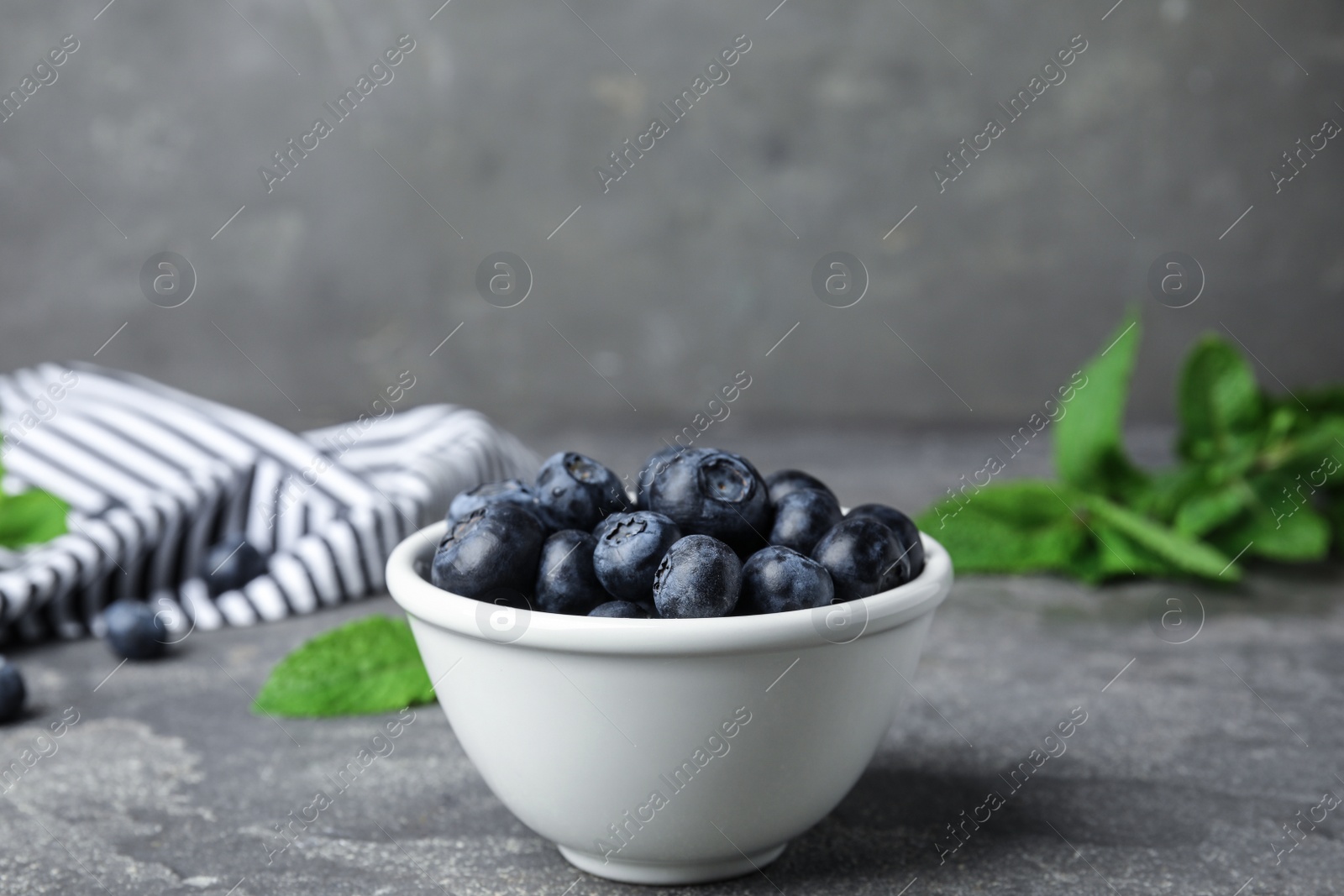 Photo of Bowl of tasty blueberries on grey stone surface
