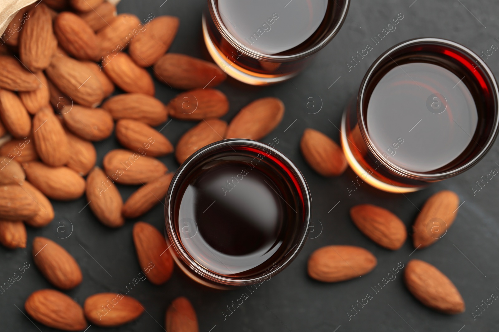 Photo of Glasses with tasty amaretto liqueur and almonds on dark gray table, flat lay