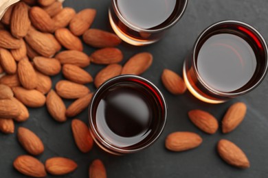 Glasses with tasty amaretto liqueur and almonds on dark gray table, flat lay