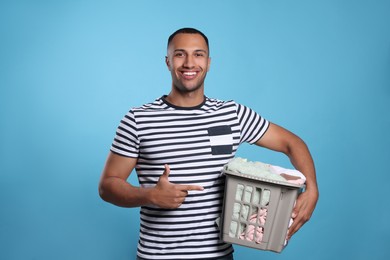 Photo of Happy man with basket full of laundry on light blue background