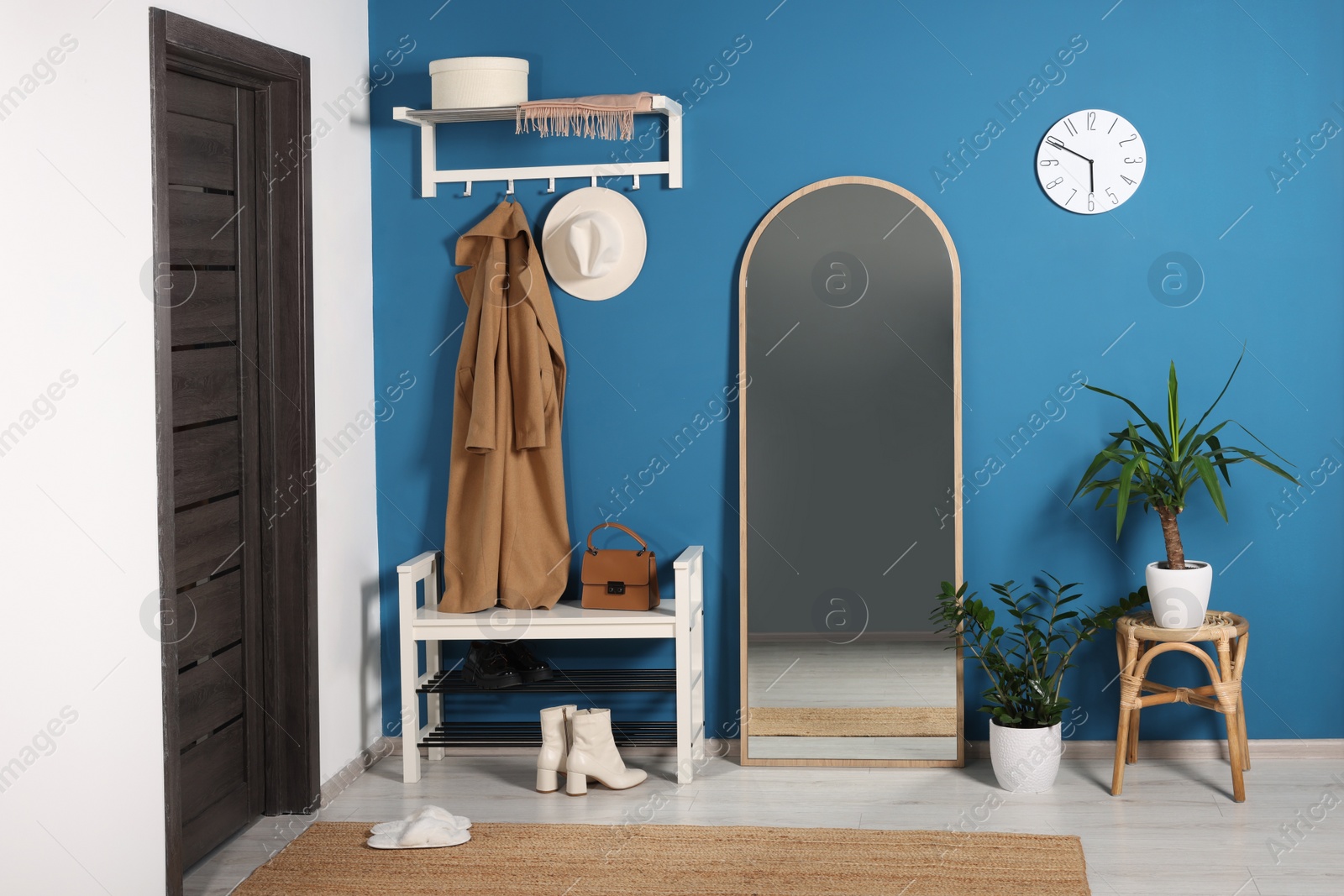 Photo of Stylish hallway with shoe storage bench and mirror near blue wall. Interior design