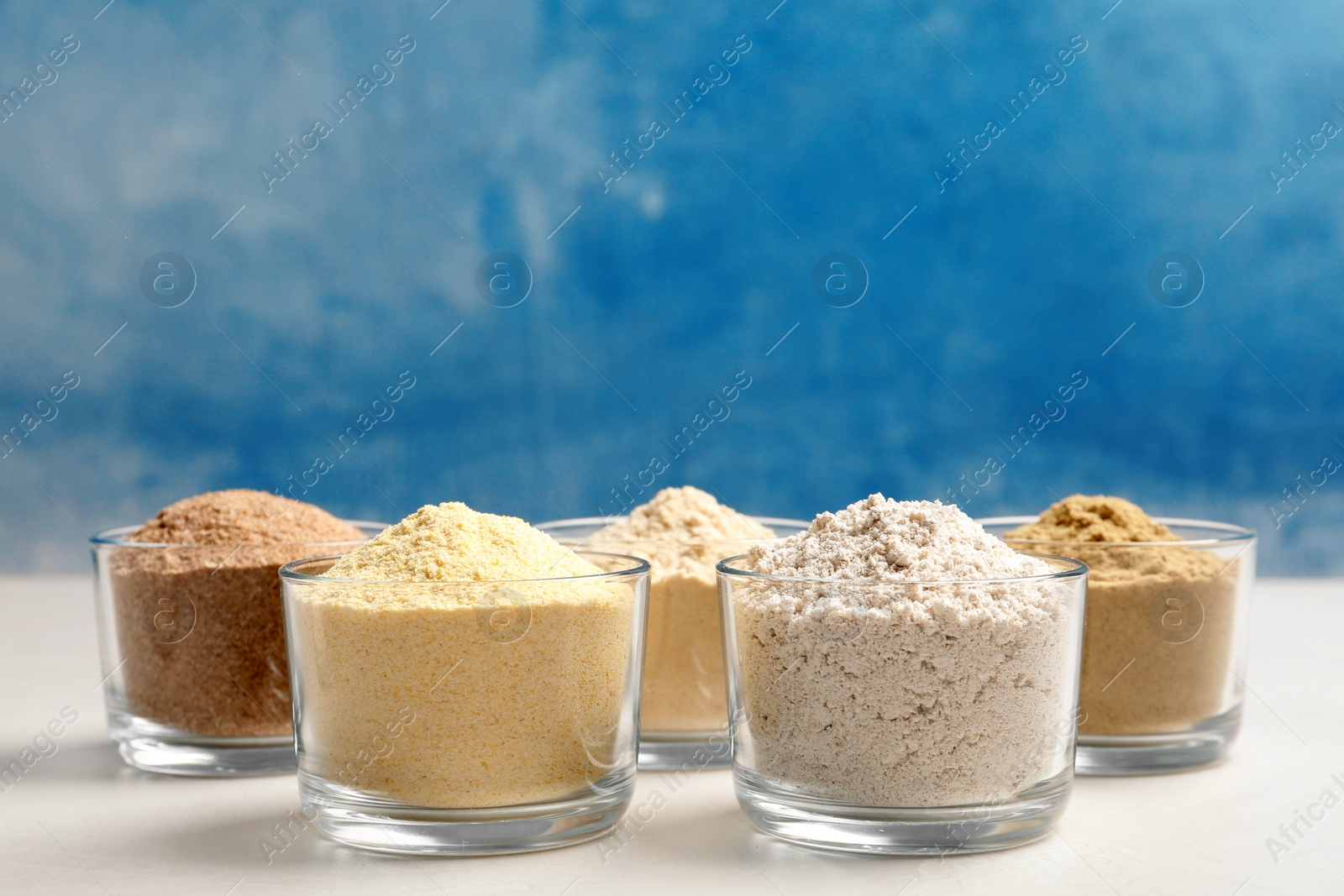 Photo of Bowls with different types of flour on table against color background. Space for text