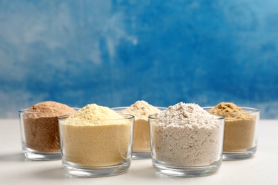 Photo of Bowls with different types of flour on table against color background. Space for text