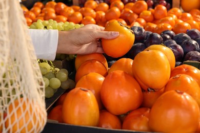 Photo of Woman picking fresh persimmon at market, closeup