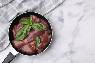 Photo of Raw chicken liver with basil in frying pan on white marble table, top view. Space for text