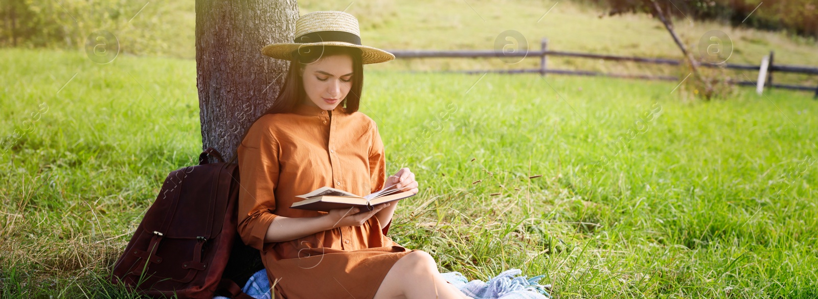 Image of Young woman reading book under tree on meadow. Banner design