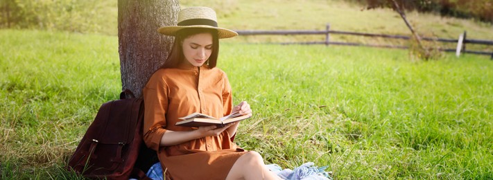 Image of Young woman reading book under tree on meadow. Banner design