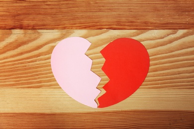 Photo of Halves of cut paper heart on wooden background, top view. Relationship problems