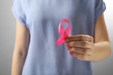 Photo of Woman with pink ribbon on light grey background, closeup. Breast cancer awareness