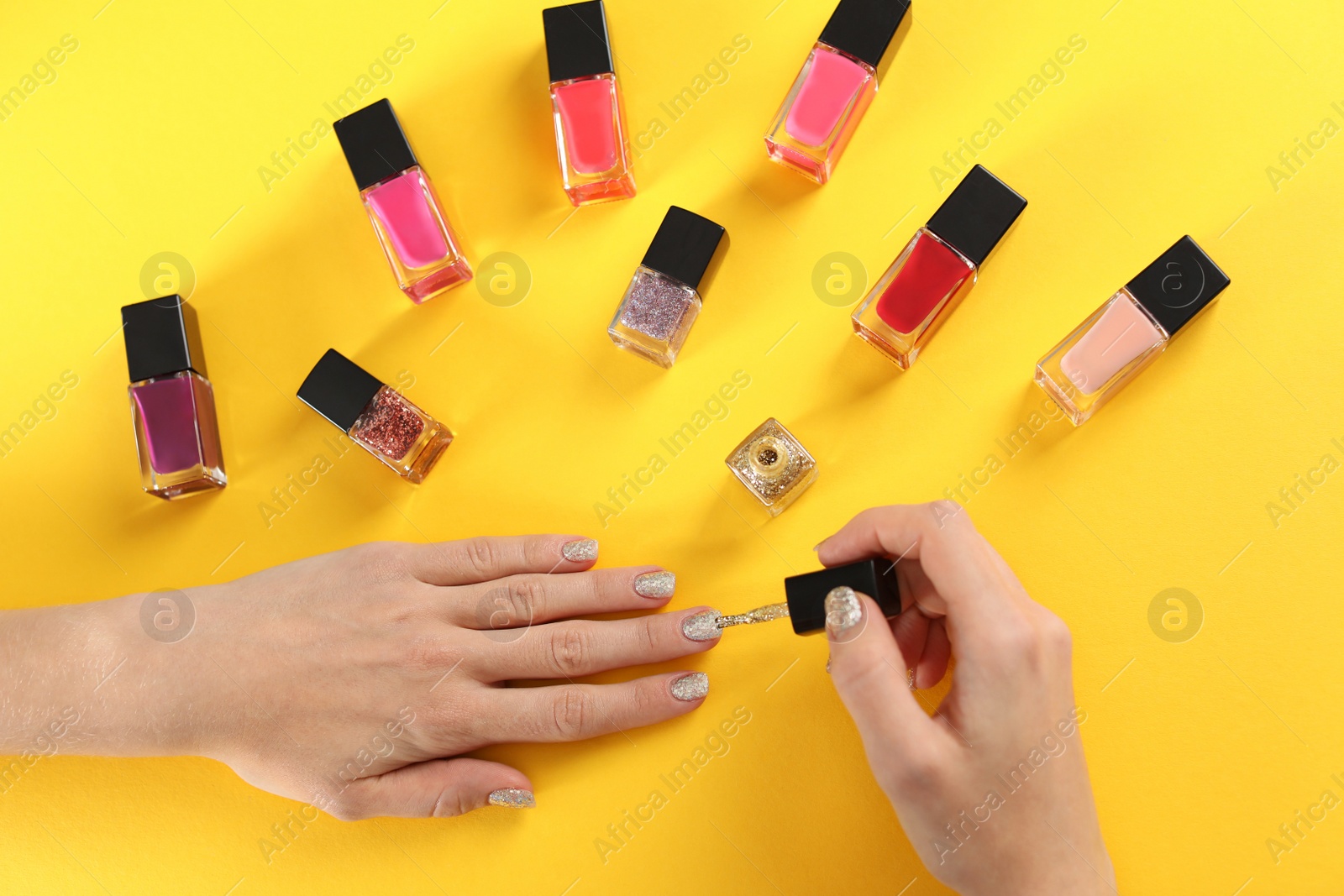 Photo of Woman applying nail polish on color background, top view