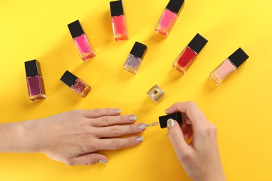 Photo of Woman applying nail polish on color background, top view