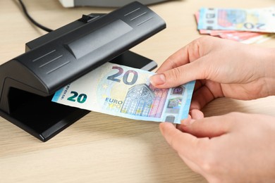 Photo of Woman checking Euro banknote with currency detector at wooden table, closeup. Money examination device