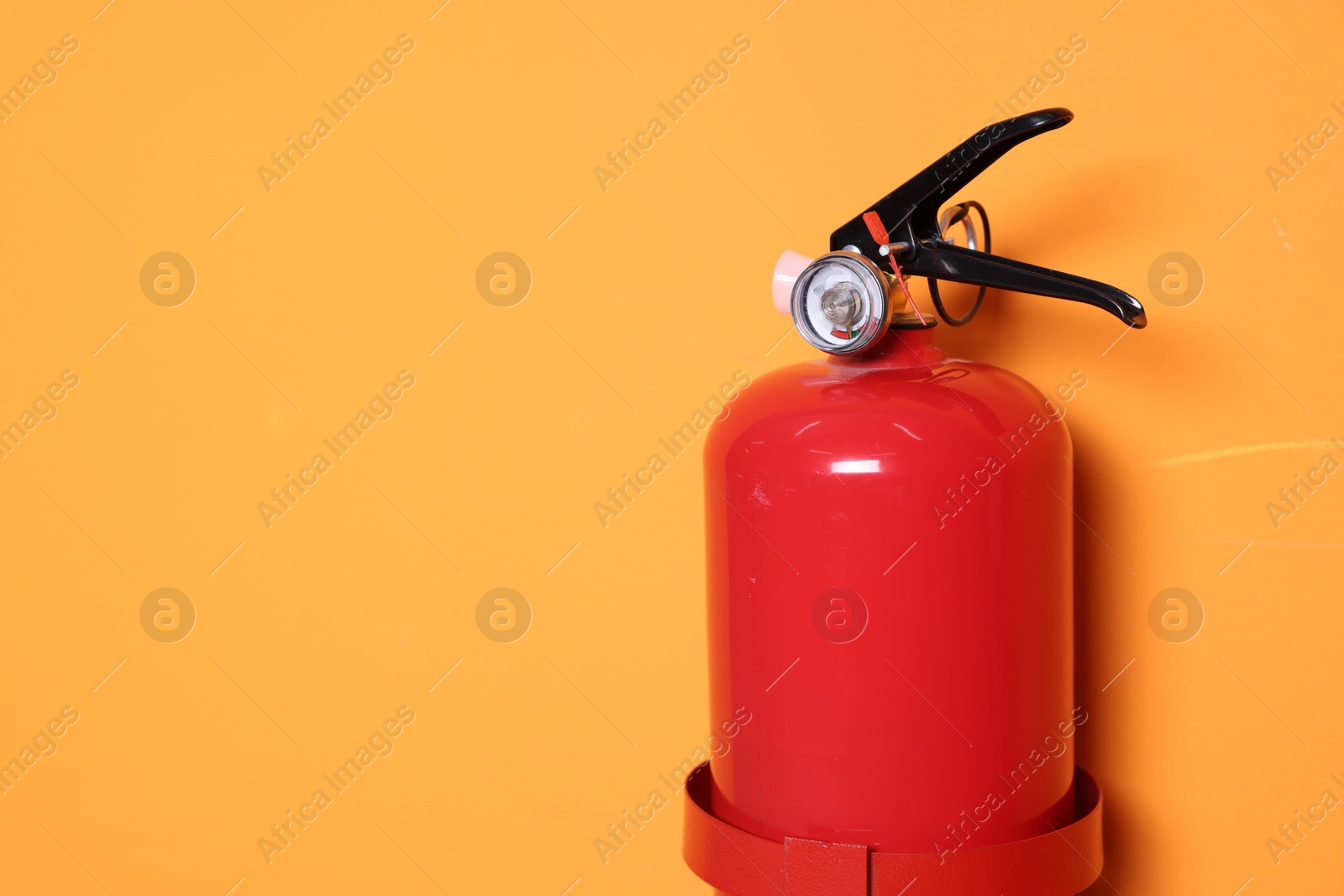 Photo of Red fire extinguisher on orange background. Space for text