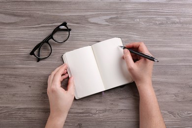 Photo of Woman writing in notebook at wooden table, top view