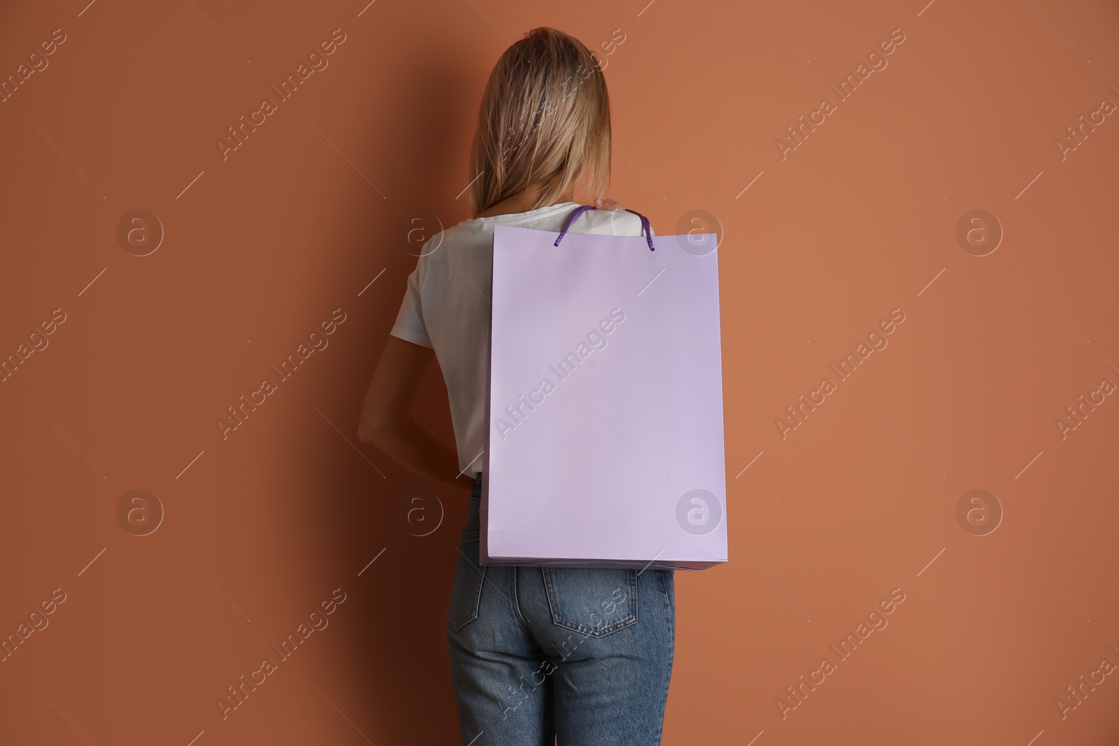 Photo of Woman with paper shopping bag on light brown background, back view
